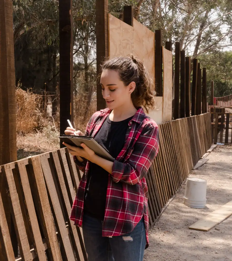 A woman writing notes on a clipboard beside a wooden fence